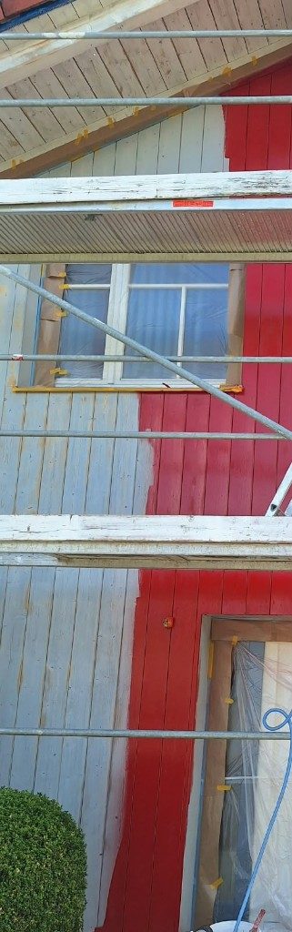 Holzfassade, links noch grau, rechts bereits kräftig rot gestrichen