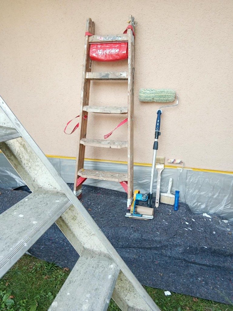 Leiter, Farbroller und Pinsel vor einer frisch gestrichenen Wand