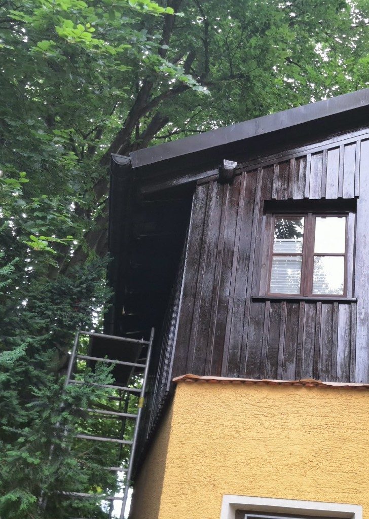 Dunkle Holzschalung über kräftig gelbem Putz