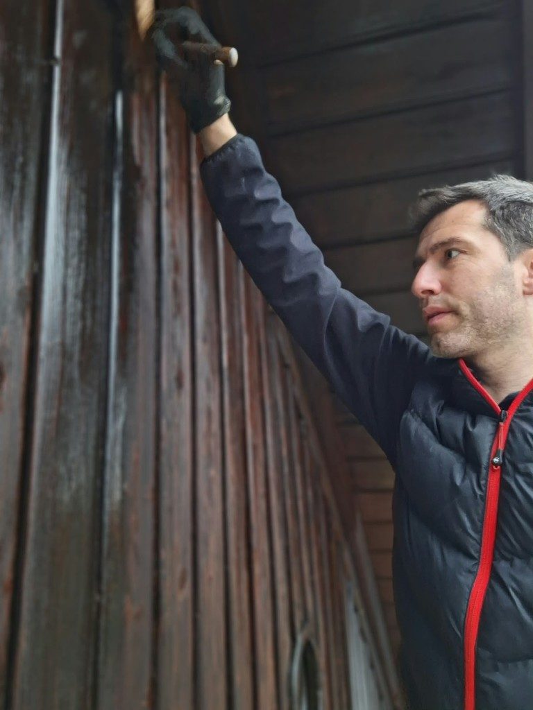 Lasur wird mit dem Pinsel auf dunkle Holzschalung aufgetragen